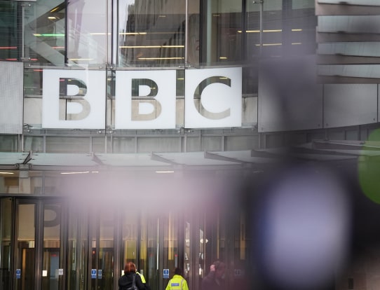 The entrance to the BBC headquarters, with the large BBC logo displayed above glass doors.