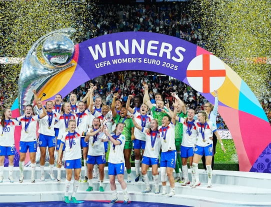 The England women’s football team celebrate under a “Winners UEFA Women’s Euro 2025” arch, lifting the trophy amid confetti.