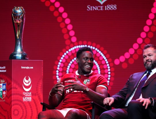 Maro Itoje smiling on stage beside a trophy during a rugby event.